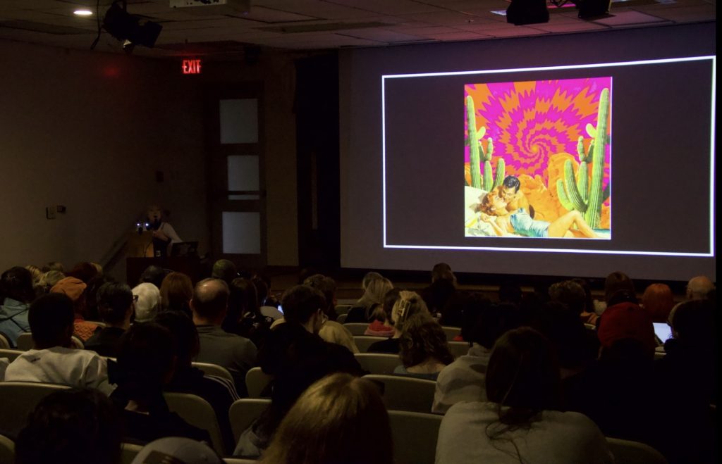 Photo of a PowerPoint slide that shows a man and woman on a bed surrounded by cactus with a pink and yellow spiral in the background.