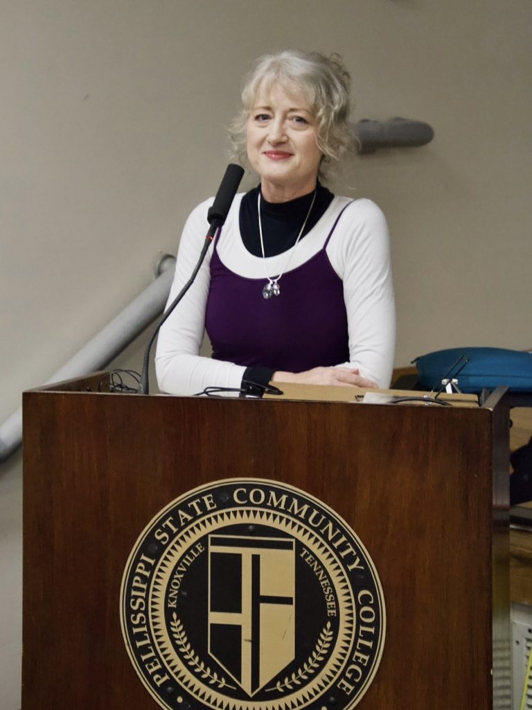 Dr. Annie Gray stands at a lectern and looks at the camera.